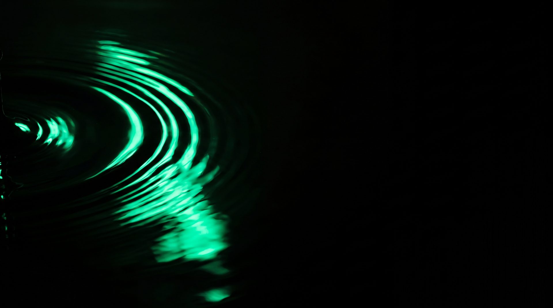 Dark still water surface with slow concentric ripples lit by a single emerald beam